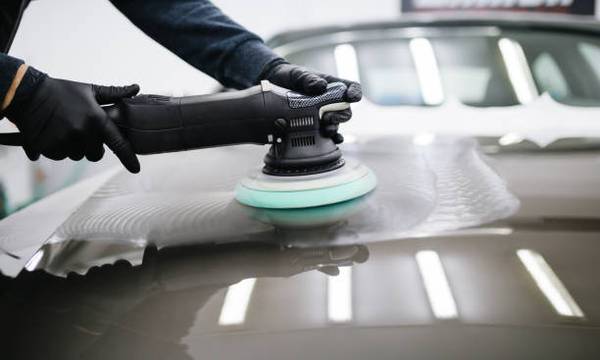 Photo of person's hands wearing black gloves holding a cut and compound hand machine overtop of the surface of a black car.